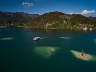 Loď pluje po Wolfgangsee, modrém jezeře obklopeném zalesněnými kopci a ostrůvky pod jasnou oblohou.