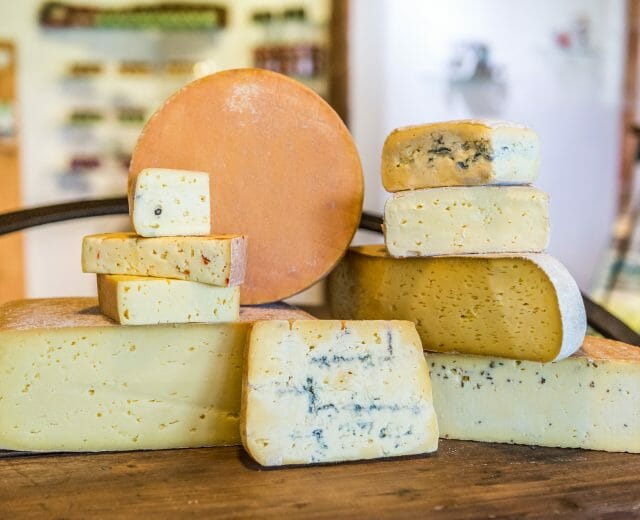 Na dřevěném stole v rustikálním prostředí jsou naskládány různé řemeslné sýry Pinzgau.