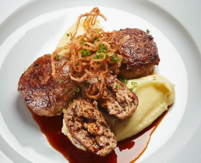 Tři masové placičky z maso-vepřové a hovězí s omáčkou, bramborovou kaší, křupavou cibulkou a pažitkou.