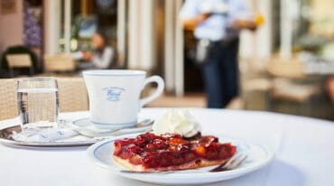 Porce švestkového koláče s kopečkem šlehačky, hrnkem kávy a skleničkou vody ve vyhlášené salcburské kavárně Café-Konditorei Fürst