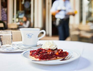 Porce švestkového koláče s kopečkem šlehačky, hrnkem kávy a skleničkou vody ve vyhlášené salcburské kavárně Café-Konditorei Fürst