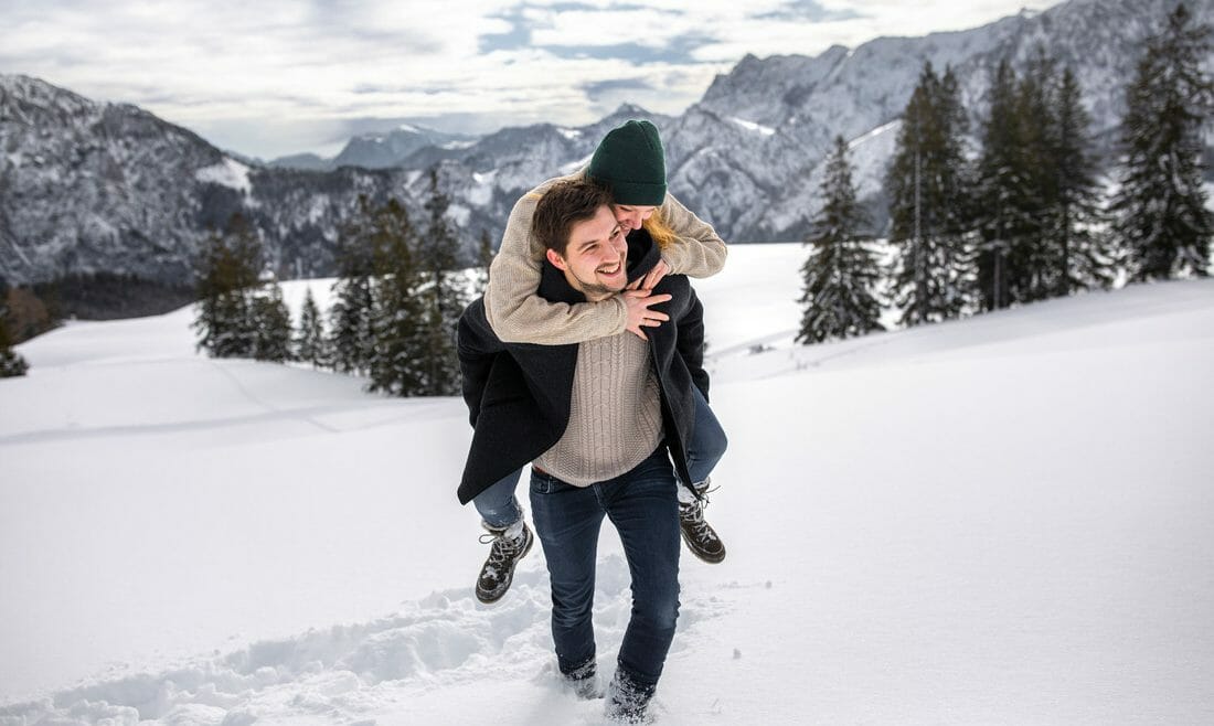 Muž jde hlubokým sněhem a nese na zádech smějící se ženu