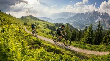 Jízda na horském kole po trase mezi zelenými pastvinami v kopcích regionu Hochkönig