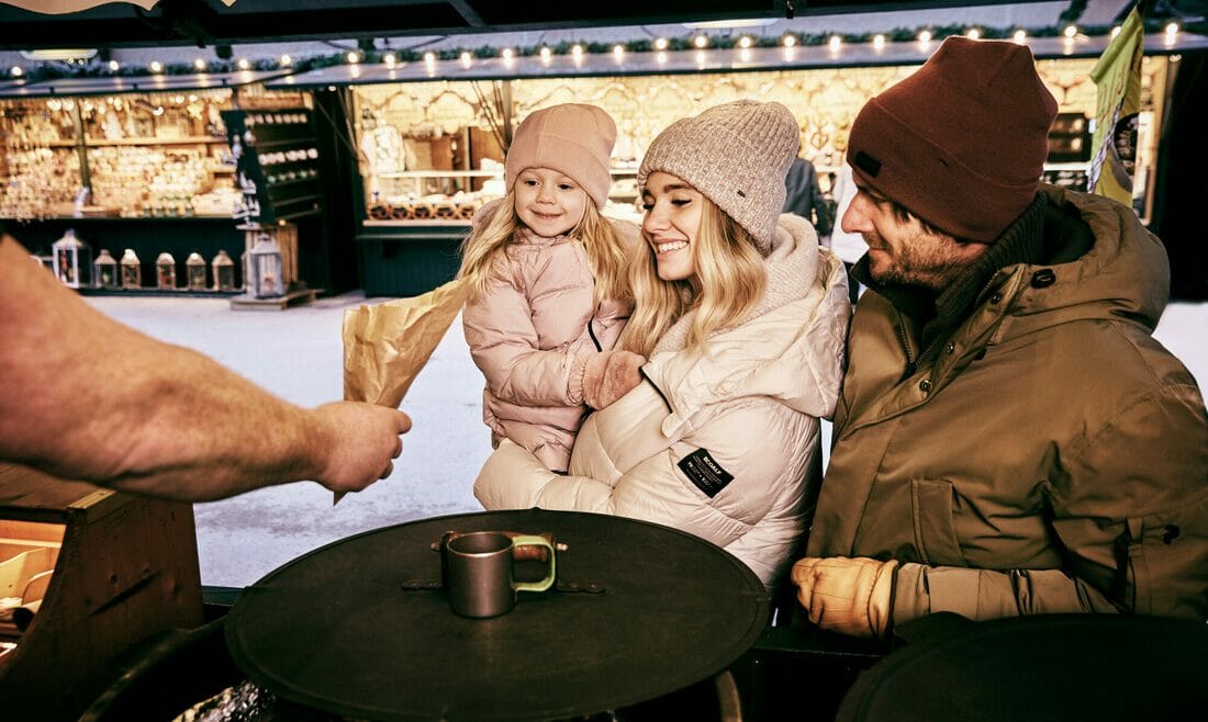 Rodina s malou dcerou kupuje pečené kaštany do kornoutku u jednoho ze stánků na vánočním trhu v centru Salcburku