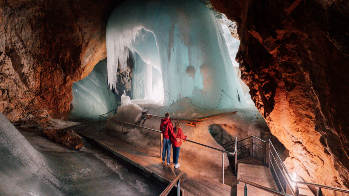 Dva lidé stojí uvnitř osvětlené ledové jeskyně Eisriesenwelt