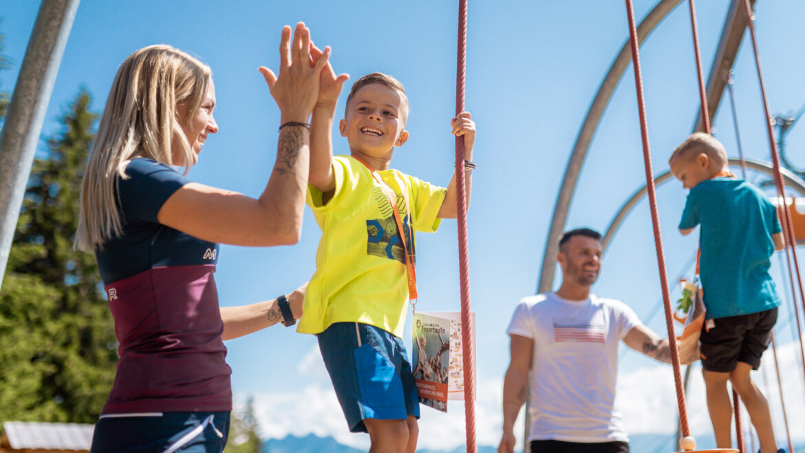 Schmidolinův křest ohněm na Schmittenhöhe © Zell am See-Kaprun Tourismus, Branislav Rohal Žena si plácá s dítětem, které šplhá po laně venku na dovolená s dětmi Salcbursko. (Zvětšený pohled)