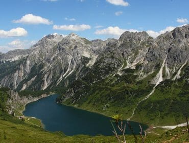 Horské jezero ideální pro turistyka, obklopen zelenými kopci a vrcholy pod modrou oblohou s rozptýlenými mraky.