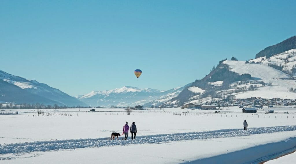 Chodci na procházce se psem obdivují barevné balóny na obloze a cestující si z balónu užívají výhled na hory