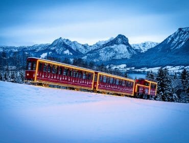 Vánočně vyzdobená zubačka SchafbergBahn jede na horu Schafberg zasněženou krajinou