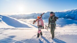 Dva lidé v lyžařské výstroji jdou po zasněžené hoře - ideální pro kurz lyžování nebo zimní rodinná dovolená Salcbursko.