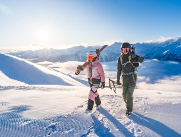 Dva lidé v lyžařské výstroji jdou po zasněžené hoře - ideální pro kurz lyžování nebo zimní rodinná dovolená Salcbursko.
