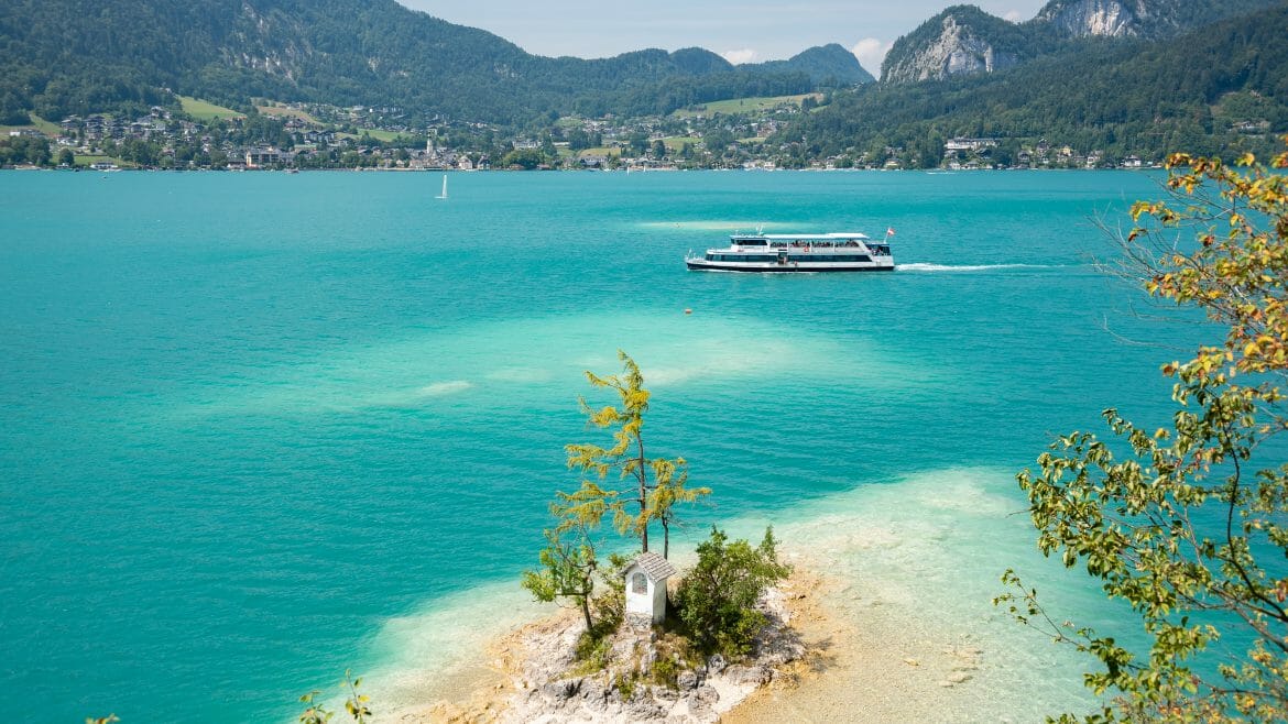 Po tyrkysově modré hladině jezera Wolfgangsee v Salzkammergut pluje moderní výletní loď mezi městy St. Gilgen a Strobl