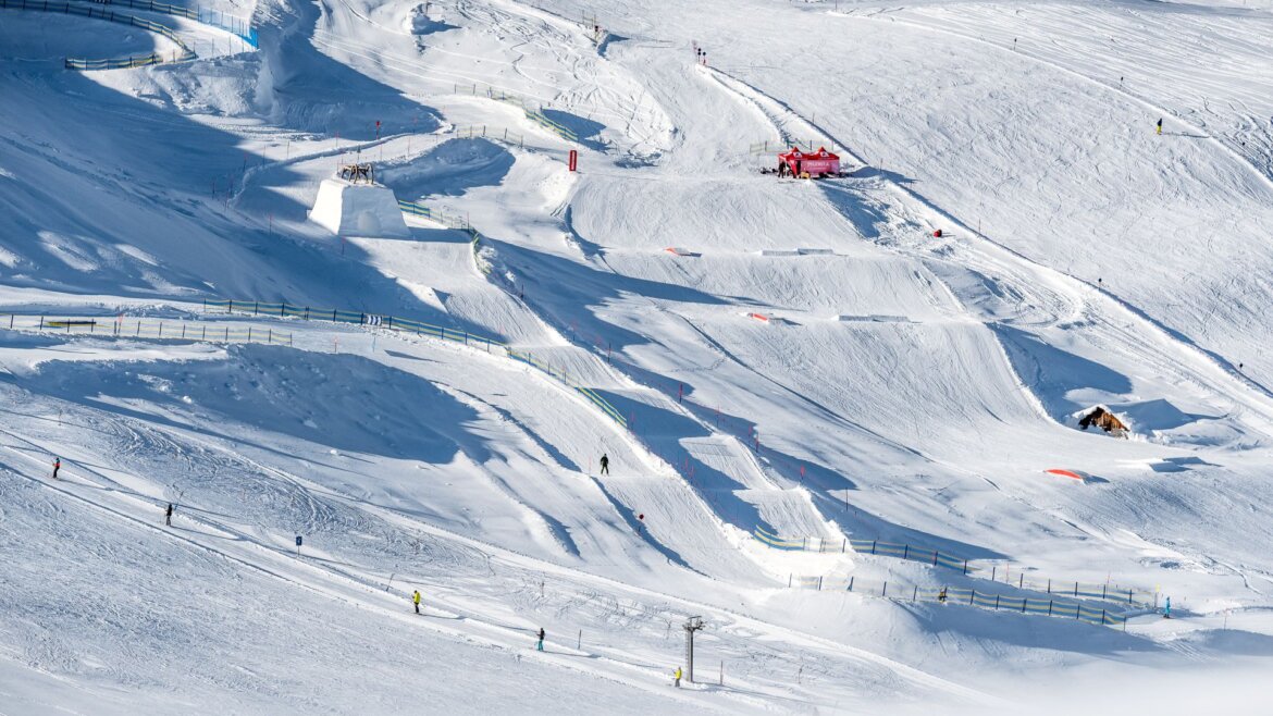 Zasněžený lyžařský terénní park ve Wildkogel Areně Neukirchen Bramberg s rampami, skoky a lyžaři pod jasnou oblohou.