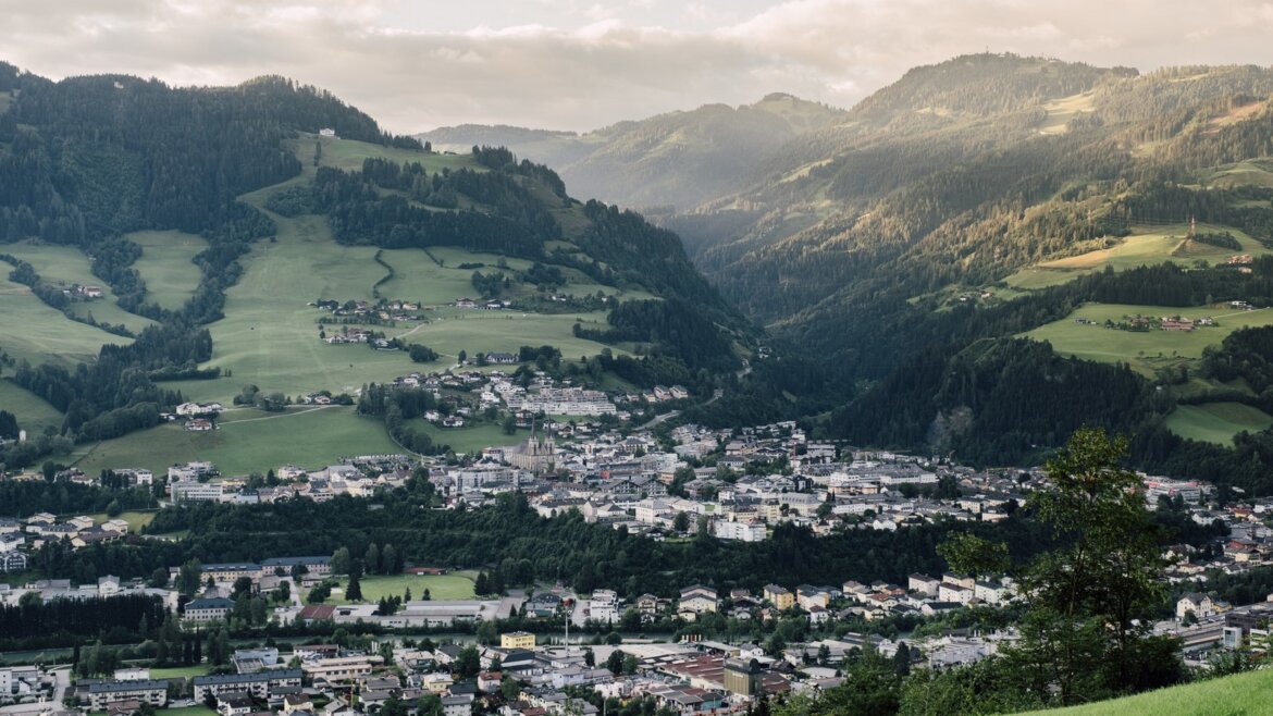 Městečko St. Johann v zeleném horském údolí pod částečně zataženou oblohou v Salcbursku. (Zvětšený pohled)