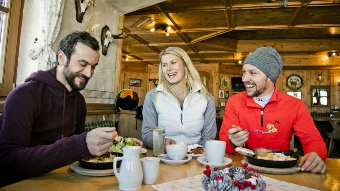 Přátelé společně stolují v tradičním alpském hostinci a ke kávě nebo čaji nesmí chybět císařský trhanec