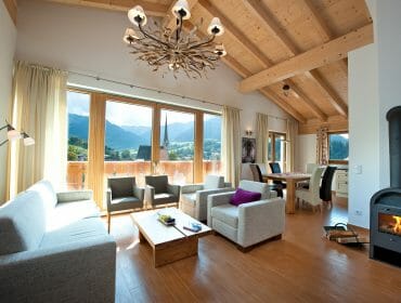 Moderní obývací pokoj s velkými okny, výhledem na hory, dřevěným stropem, osvětleným krbem -ideální zima bydlení.