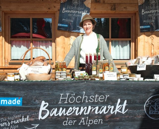 Žena stojí za stánkem s místními produkty na farmářském trhu v Alpách.