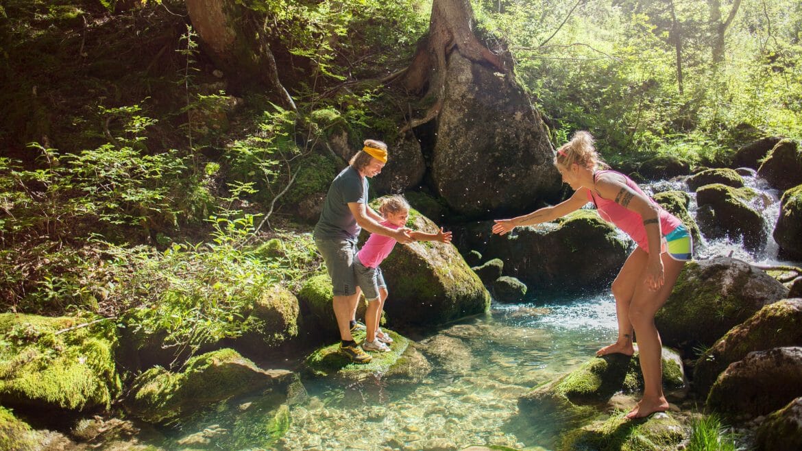 Rodina na výletě překračuje po kamenech čistý potok v Salcburském Saalachtalu