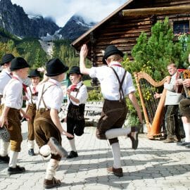 Chlapci v tradičních kožených kalhotách, bílých podkolenkách a kloboucích tančí za zvuku lidové hudby na oslavách dožínek