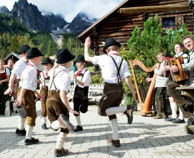 Bauernherbst Fest mit Kinder Chlapci v tradičních kožených kalhotách, bílých podkolenkách a kloboucích tančí za zvuku lidové hudby na oslavách dožínek