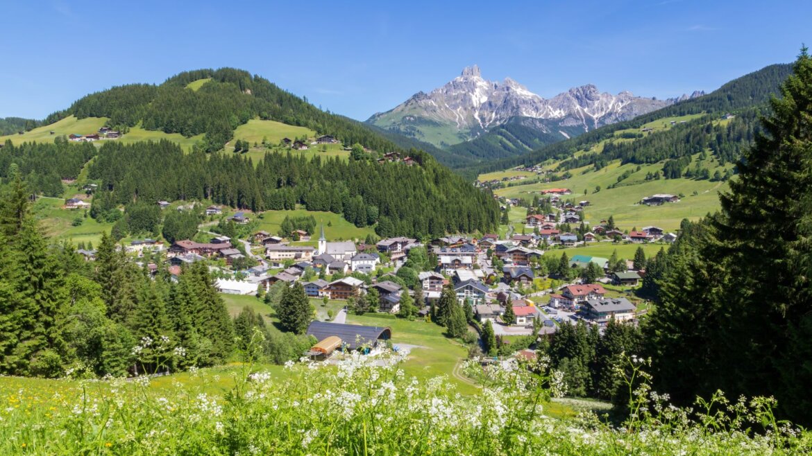 Horská vesnice Filzmoos Salcbursko se zelenými kopci, domy a zasněženými vrcholky pod jasně modrou oblohou.