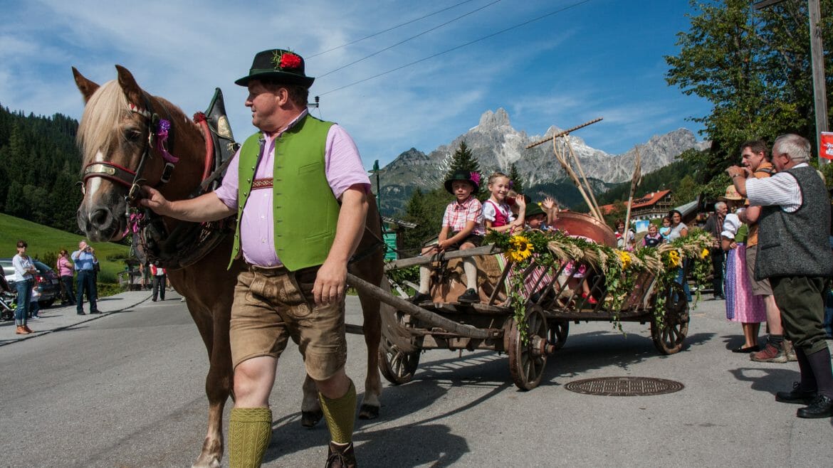 Sedlák v tradičním rakouském oděvu vede koně, který táhne květinami ozdobený žebřiňák