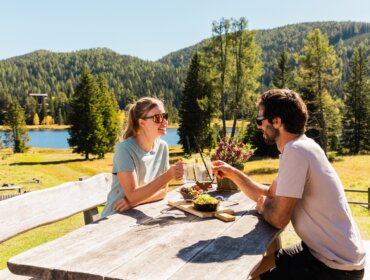Dva lidé se skleničkami u venkovního stolu ve slunném Salcburském Lungau