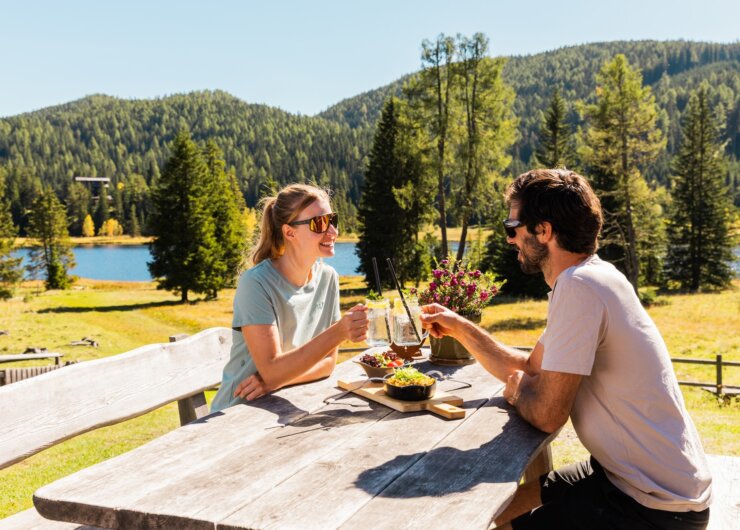Kulinarik-Salzburger Lungau Dva lidé se skleničkami u venkovního stolu ve slunném Salcburském Lungau