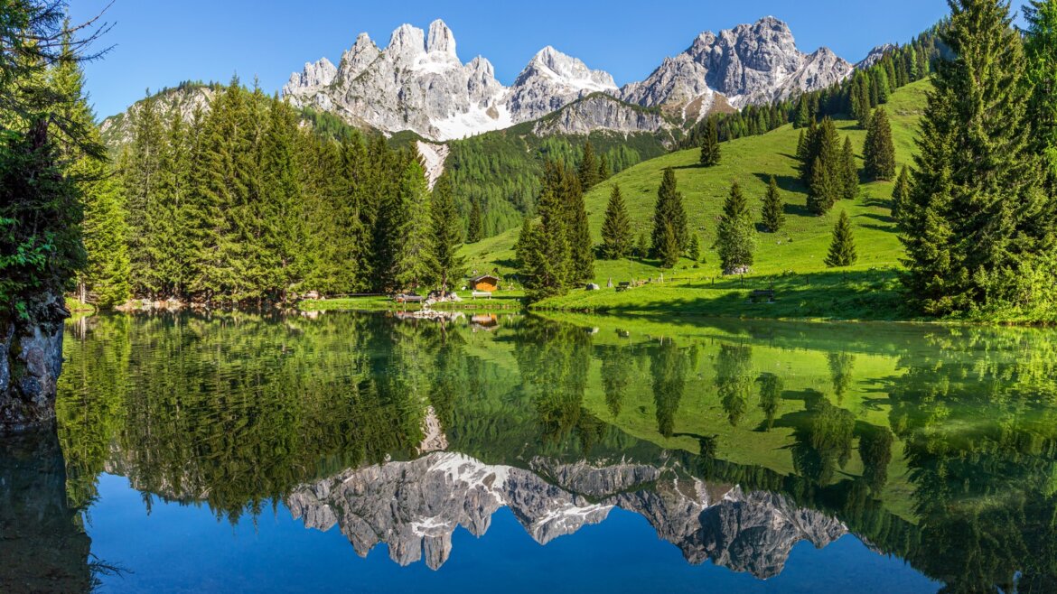 Průzračné jezero Almsee odráží za jasného slunečného dne skalnaté vrcholy Bischofsmütze, stromy a zelené pastviny