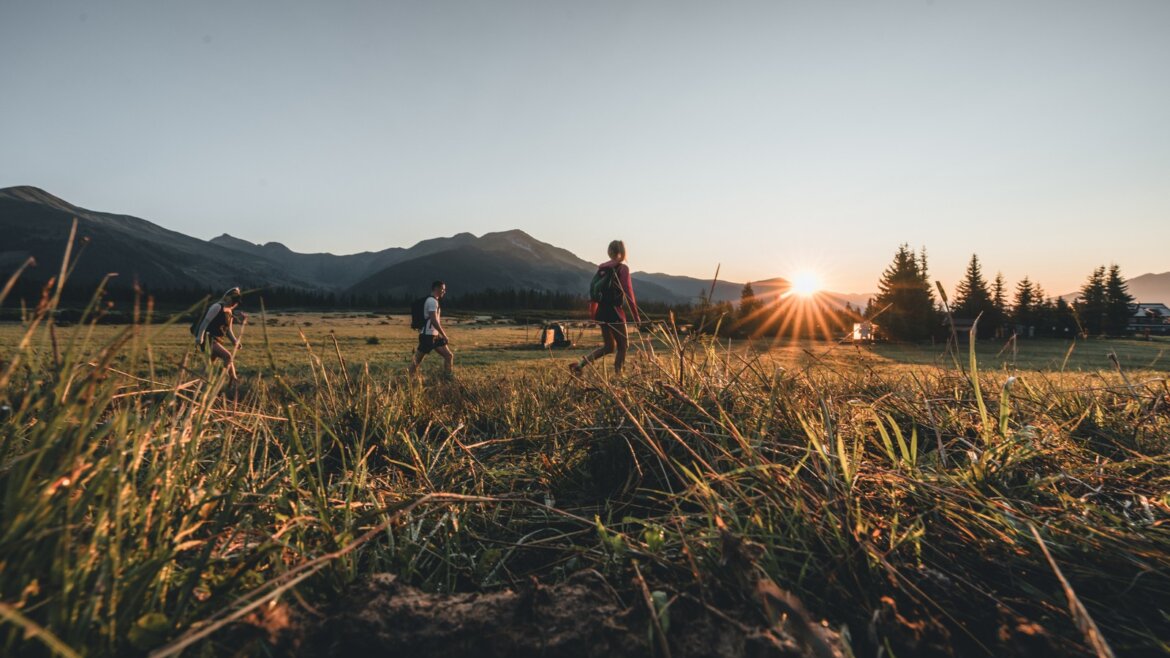 Lidé na túře v Národním parku Vysoké Taury s travnatými poli, horami a stromy kolem.