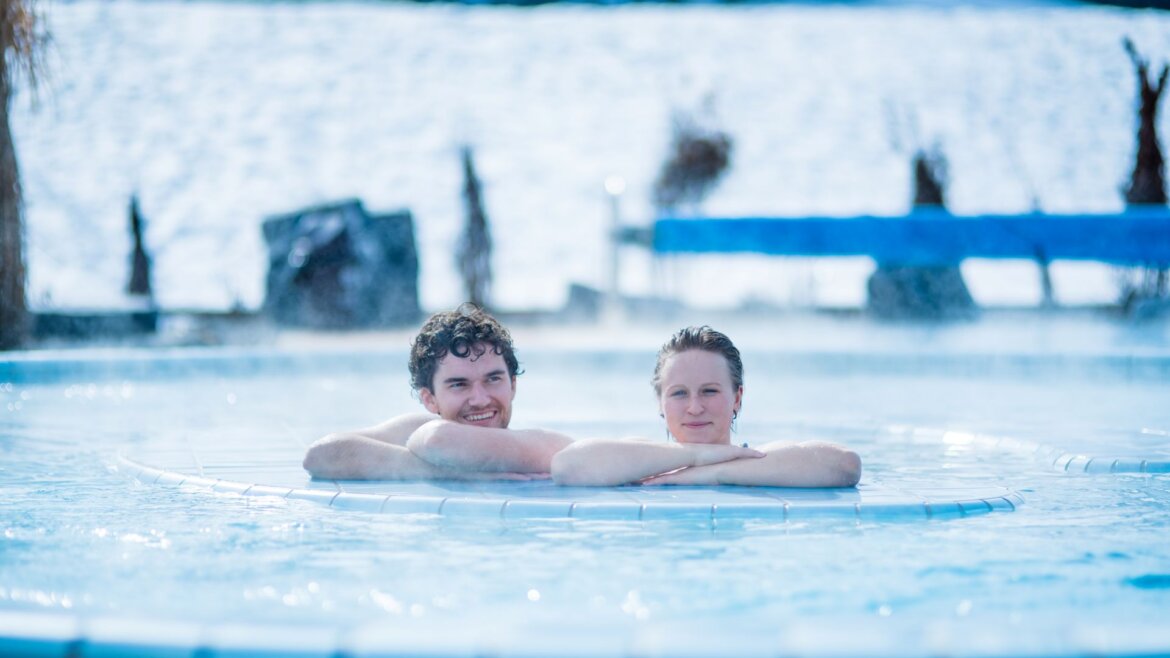 Dva lidé relaxují ve venkovním bazénu a užívají si Salcburský sportovní svět v zimě s výhledem na zasněžené okolí. (Zvětšený pohled)