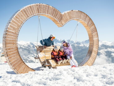 Rodina na dřevěné houpačce uprostřed zasněžených kopců Vysokých Taur v Grossarltalu