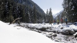 Skupina si užívá zasněženou půdu u řeky v zalesněné horské krajině arény Zima Wildkogel.