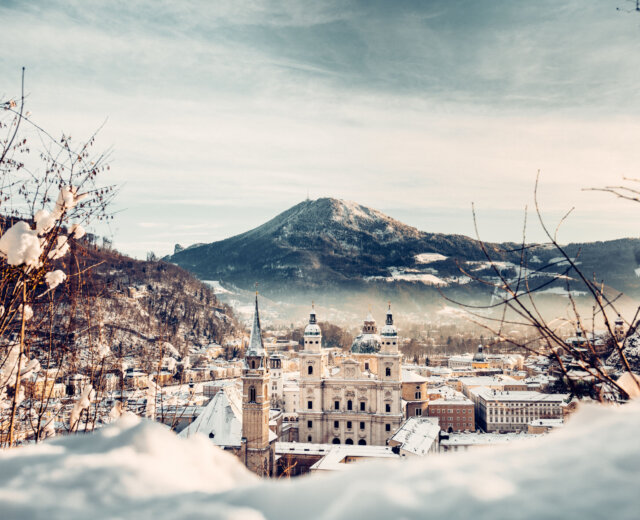 Zasněžená krajina města s katedrálou, horami a Akce v Salcbursku v zimním dni.