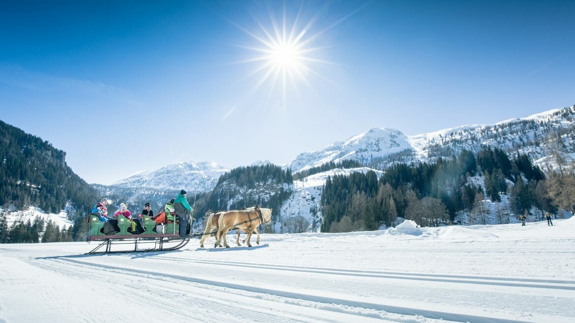 Romantická vyjížďka za slunečného dne na saních tažených koňmi v idylické krajině hor v Obertauern