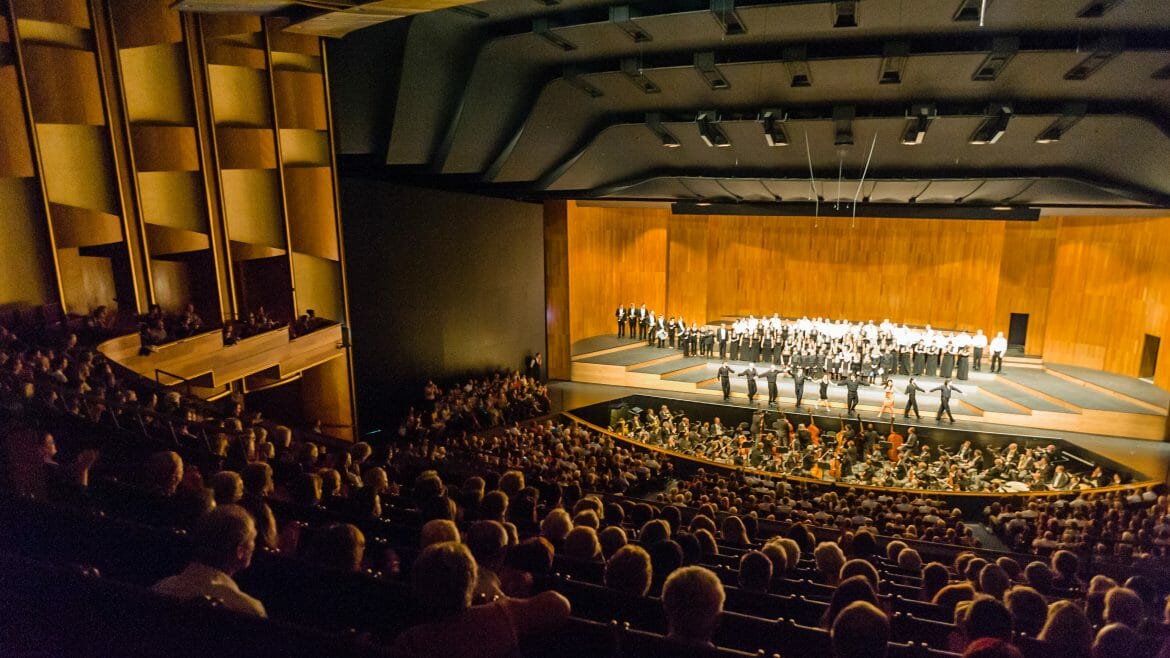 festspiele_gr_festspielhaus_tsg-1170×658 Početné publikum sleduje živé vystoupení orchestru a sboru na Salcburském festivalu v moderním koncertním sále.