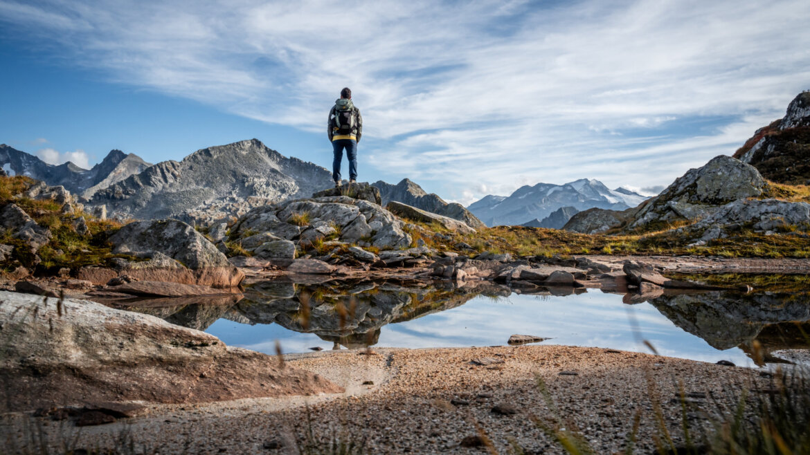 Turista stojí na skalnatém vrcholu v Grossarltal v Salcbursku v létě s výhledem na hory a průzračnou tůň.