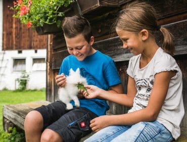 Děti krmí na lavičce farmy v Salcbursku bílého králíka