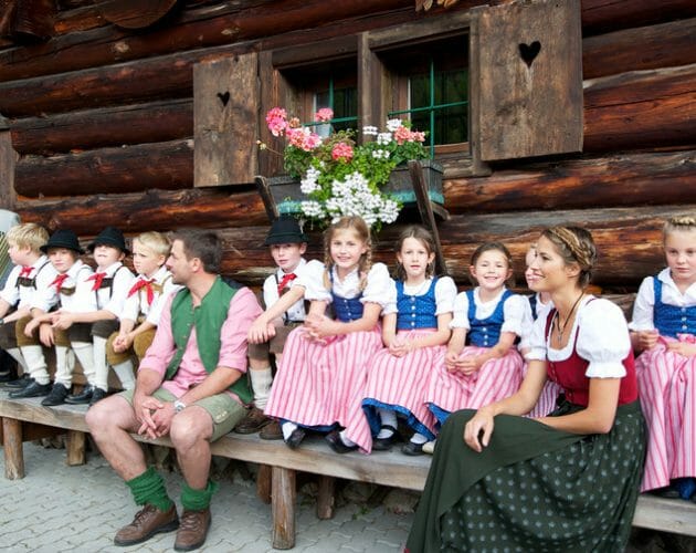 Farmářský podzim a dožínky v Salcbursku jsou plné tradičních akcí. Děti v krojích sedí na lavičce před dřevěnou chalupou a poslouchají lidovou hudbu.
