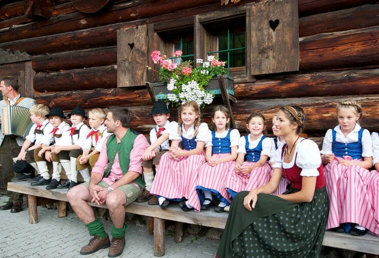 Farmářský podzim a dožínky v Salcbursku jsou plné tradičních akcí. Děti v krojích sedí na lavičce před dřevěnou chalupou a poslouchají lidovou hudbu.
