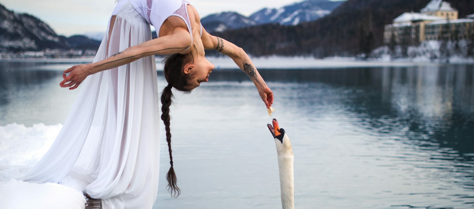 Jako v zimní pohádce. Žena v bílých šatech se naklání z mola u jezera Fuschlsee a krmí labuť