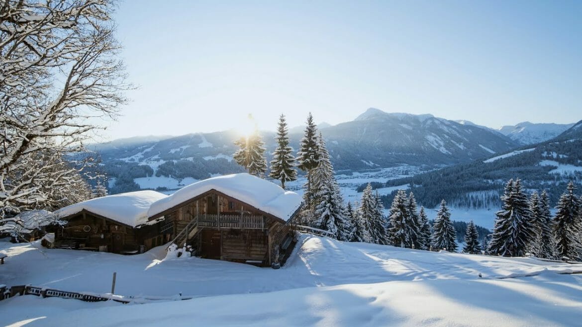 Hluboký neporušený sníh a bílá sněhová čepice na střeše dřevěné salaše se třpytí v zimním slunci, které zapadá za bílé štíty hor