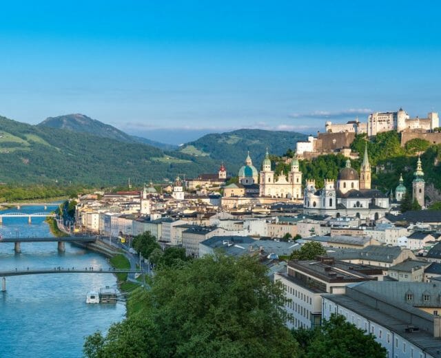 Výhled z Mnišské hory na Salcburk, panorama města se střechami historických domů, kostelů, pevností Hohensalzburg, okolo nichž se vine řeka Salzach