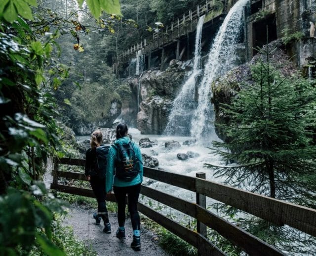 Dva lidé jdou po lesní cestě kolem vodopádu a starého stavení a prozkoumávají svěží zeleň na Kartě Salcburské.