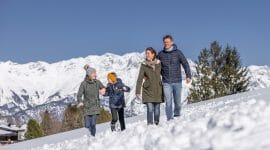 Rodina na zimní procházce zasněženou krajinou s bílými horskými štíty za sebou