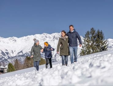 Rodina na zimní procházce zasněženou krajinou s bílými horskými štíty za sebou