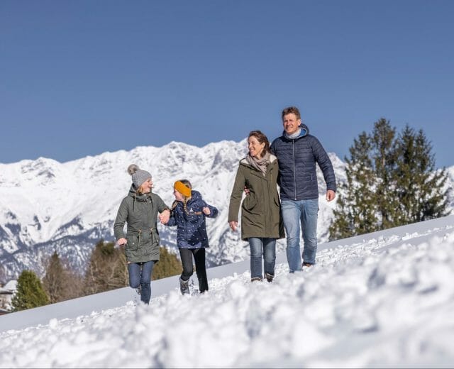 Rodina na zimní procházce zasněženou krajinou s bílými horskými štíty za sebou