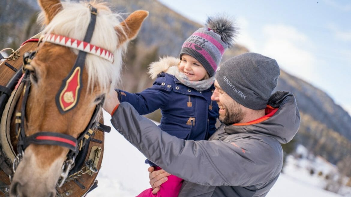 Zapřažení koně vozí návštěvníky na saních zimní krajinou Salcburského Lungau a děti si je mohou i pohladit 
