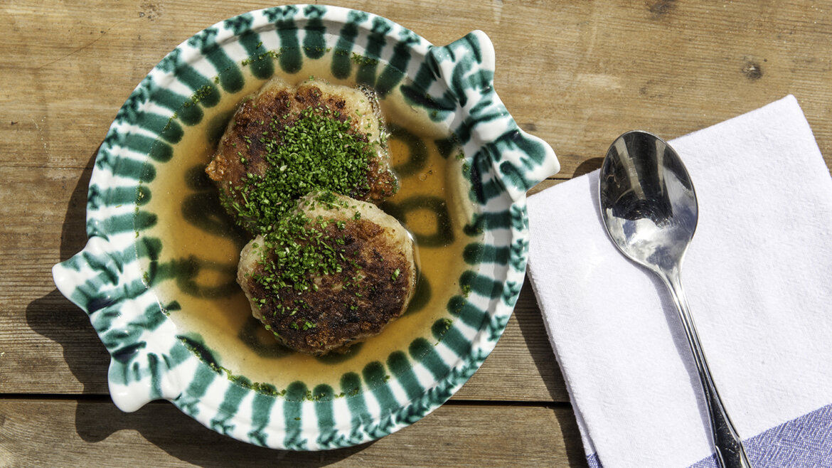 Tradiční vývar a Kaspressknödel © TVB Rauris, Florian Bachmeier Dva velké sýrové knedlíky s bylinkami v vývaru, podávané na dřevěném stole. (Zvětšený pohled)