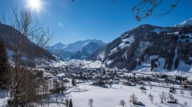 Raurisertal_Talansicht_Lila&Plietsch Zasněžená vesnice Raurisertal, zasazená v údolí pod jasným sluncem.